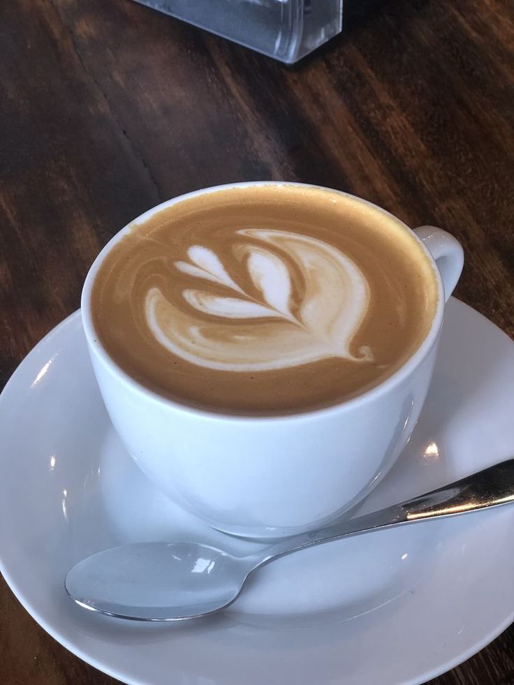 Steaming cup of coffee next to a slice of cake on a white plate atop a wooden table in a cozy cafe setting, evoking a warm and inviting atmosphere
